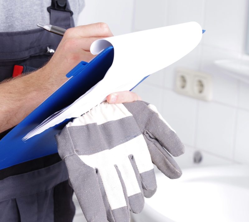 Hausmeister steht in Badezimmer mit einem Klemmbrett und dokumentiert